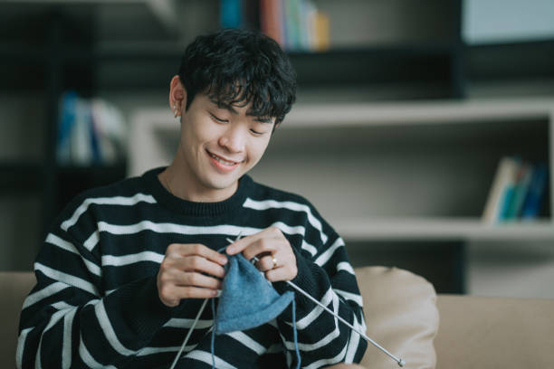 Asian Chinese Gay man knitting at home sitting on sofa in living room during weekend Asian Chinese Gay man knitting at home sitting on sofa in living room during weekend BEING HAPPY stock pictures, royalty-free photos & images