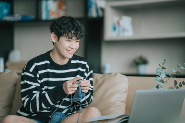 istock Asian Chinese Gay man learning knitting through online class video call using laptop in living room sitting on sofa 1438848810