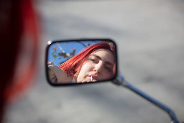 The girl uses a motorcycle mirror to look at her makeup on the street.