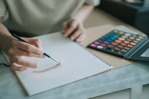 Asian Chinese Gay man make up artist practicing colouring eye shadow on paper at home in living room