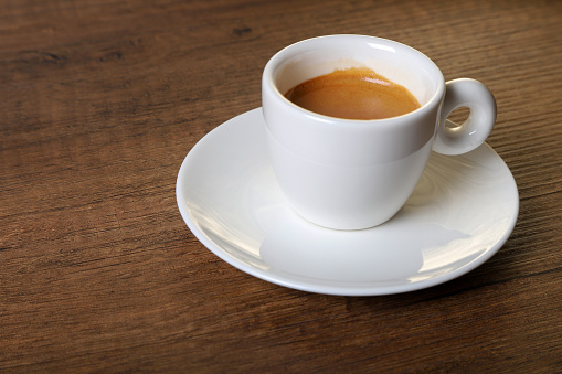 White cup of espresso with coffee beans on wooden background