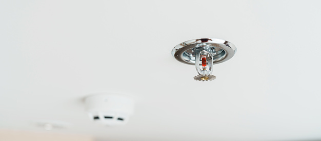Fire Sprinkler and Smoke sensor detector mounted on roof in home or apartment. Safety and conflagration security concept