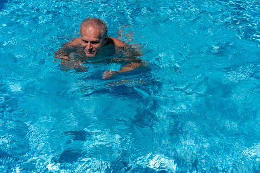 Top, front view of adult man swimming in pools blue water. He is having  vacation in Peroj, Istria on Adriatic coast. Mediterranean