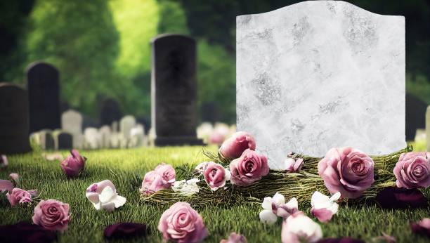 A white marble gravestone with pink roses on the ground in a graveyard