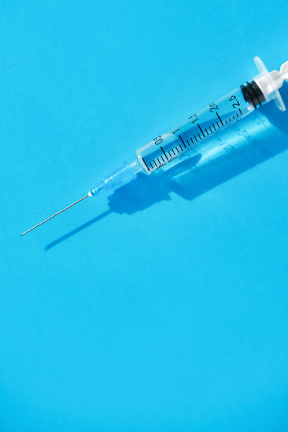 istock Disposable syringe with clean needle and liquid remedy placed on bright blue background. Flat lay, vertical image. 1438863694