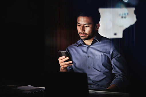 Stock trader, phone and working man at night in dark office to check forex stock market, analysis and reading data. Male entrepreneur check stock exchange value, mobile app or investment notification