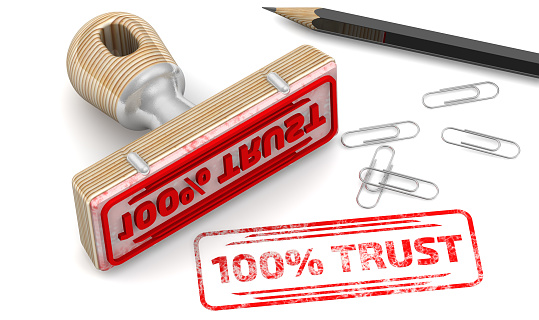 The stamp and a red imprint with text: 100% TRUST on a white surface with pencil and clips. 3D illustration