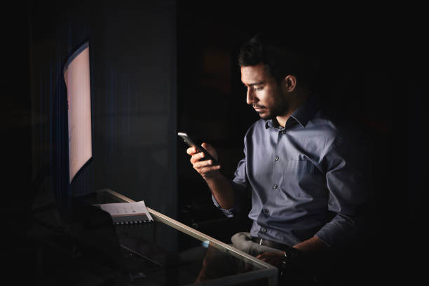 istock Businessman, work and overtime, smartphone and night, working late and check email, text or social media, technology and communication. Young, employee and dark office, computer desk and phone. 1438864664