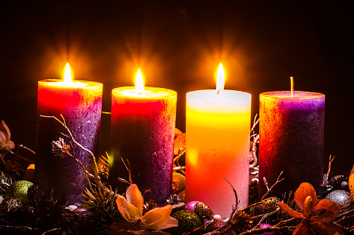 pink and purple candles in advent wreath decoration on black background