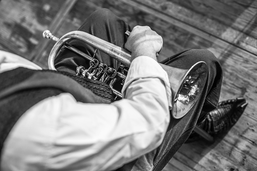 A grayscale shot of a man holding a trumpet on his lap with a blurred background