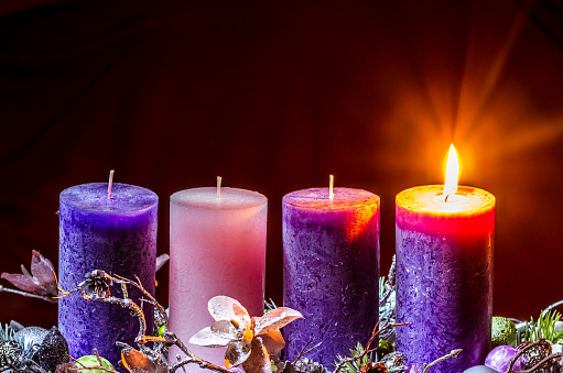 four red burning candelights and fir cones for advent or christmas decoration on blurred shiny background with copy space for holiday greetings