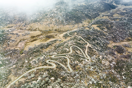 Aerial view of a winding mountain country road with desolate rocky background