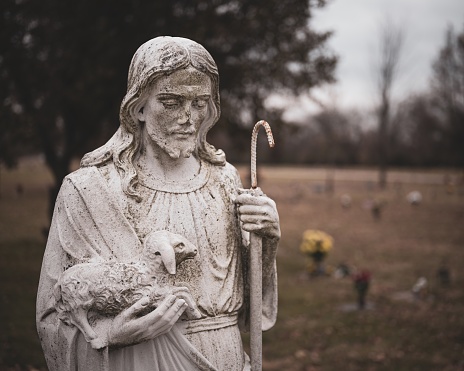 A weathered statue of Jesus Christ with a sheep in his hands on a blurred background