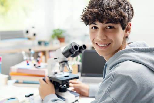Happy adolescent student using a microscope at home, science and learning concept