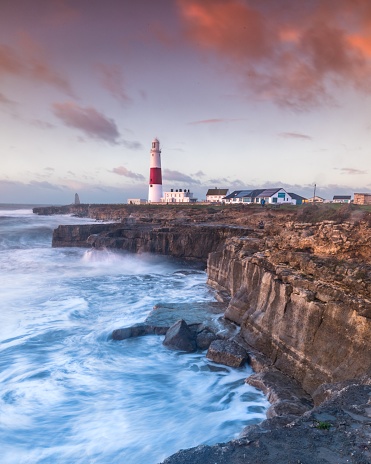 The Portland Bill lighthouse in Portland, Dorset, UK with the colors of sunrise and the waves made for a lovely swell