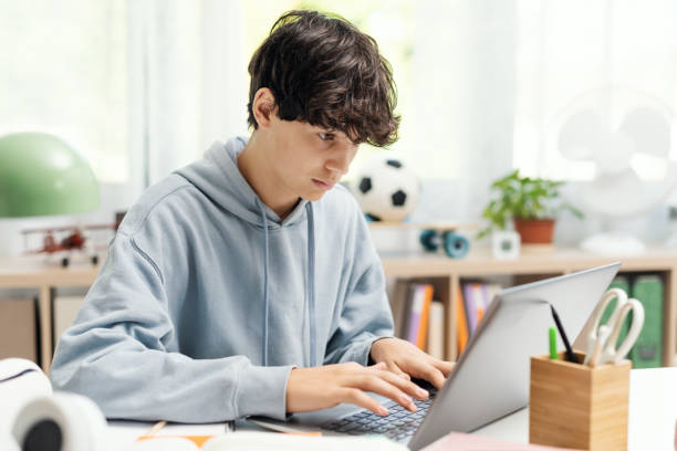 student connecting online using his laptop - alleen één tienerjongen stockfoto's en -beelden