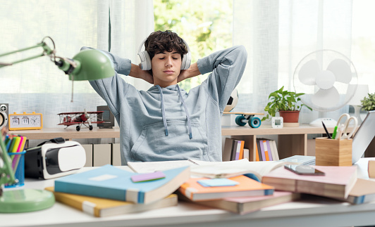 Teenager student taking a break, he is relaxing and listening to music using headphones