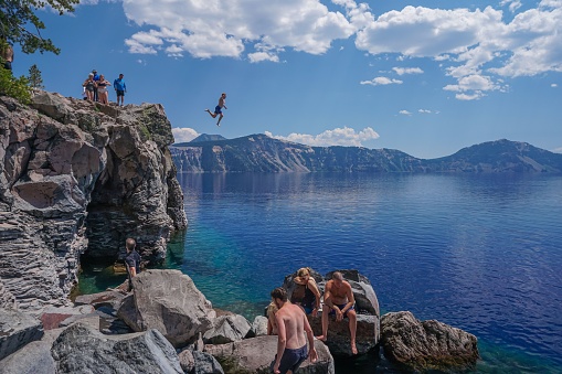 Crater Lake National Park, United States – July 29, 2022: A brave cliff jumper leaps into Crater Lake on a scenic summer day inside Crater Lake National Park.