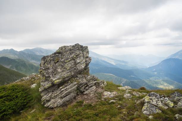 istock Rock on a hill covered in greenery with rocky mountains under a cloudy sky on the blurry background 1438871442