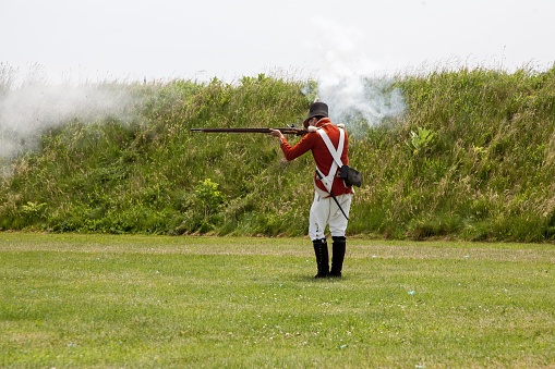Niagara on the Lake, Canada – June 20, 2019: Actor dressed like an 18th century soldier is firing a musket. Location is Fort George a historic military structure at Niagara