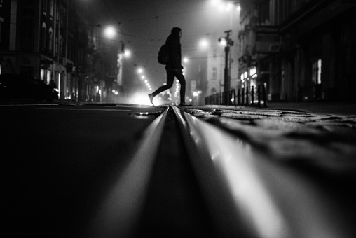 A grey scale shot of a person crossing the street at night