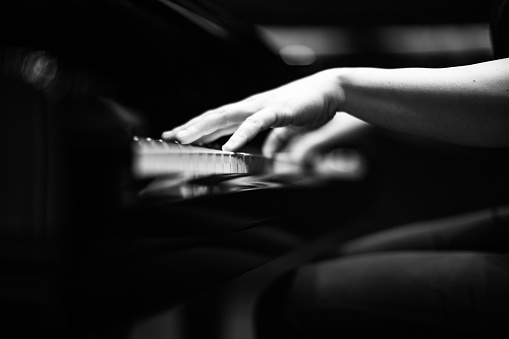A grey scale shot of a the hands of a person playing the piano