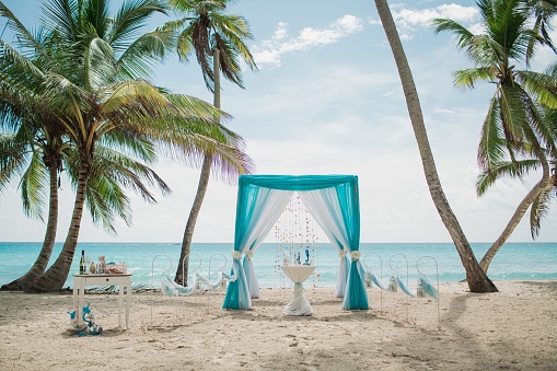 A blue and white wedding aisle in a beach surrounded by palms with the sea on the background
