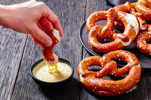 woman dips a piece of soft pretzel in cheese sauce, horizontal view from above, close-up