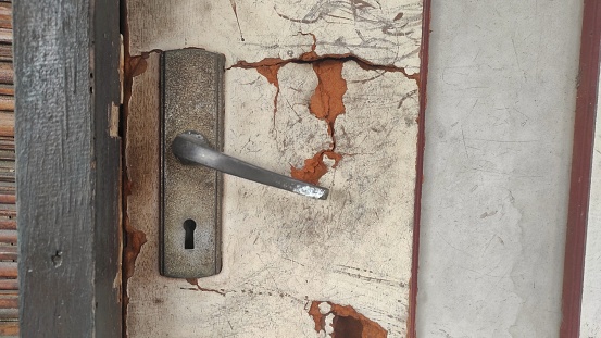 An old cracked door with rusty door knob of old house in urban area