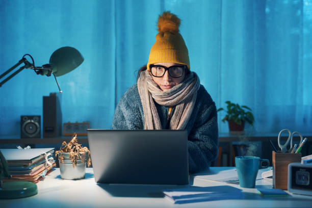 Woman feeling cold at home in winter Woman sitting at desk and feeling cold, she is wearing warm clothes and saving money on her utility bills overworked funny stock pictures, royalty-free photos & images