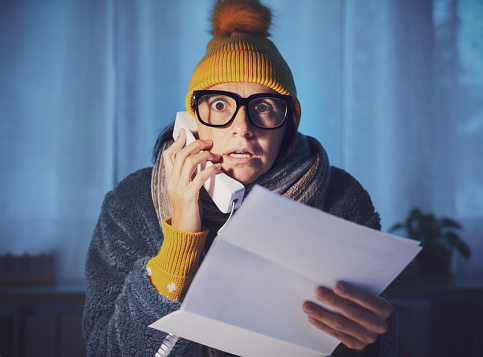 Woman feeling cold at home and checking expensive utility bills, she is calling the supplier and complaining