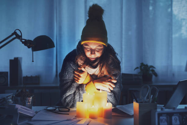 Sad broke woman feeling cold at home, she is wearing warm clothes and warming up with candles: crisis and expensive utility bills concept