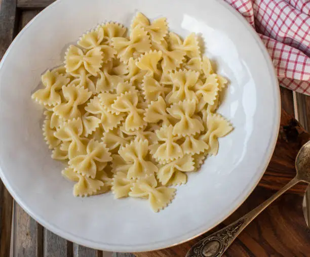 Fresh cooked bowtie noodles or farfalle on a pasta plate on wooden table background from above