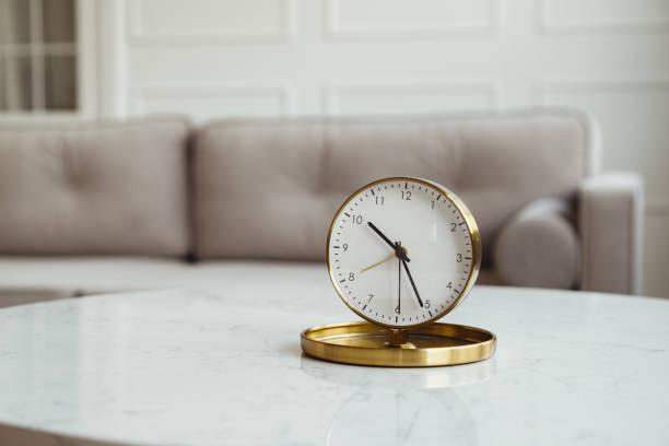 istock Table clock on a coffee table in a living room with a gray sofa. Interior of a modern apartment, details, time 1438886266