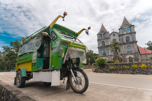 Valencia, Bohol, Philippines -  A motorela, a variant of a tricycle, is parked in front of The Parish of the Santo Niño, also known as Valencia Church. Valencia, Bohol, Philippines - May 2022: A motorela, a variant of a tricycle, is parked in front of The Parish of the Santo Niño, also known as Valencia Church. philippines tricycle stock pictures, royalty-free photos & images