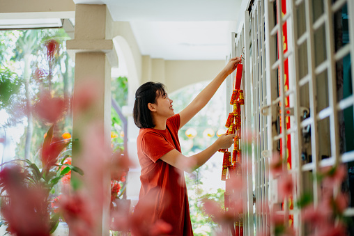 Image of an Asian Chinese woman decorating her house for Chinese New Year family reunion