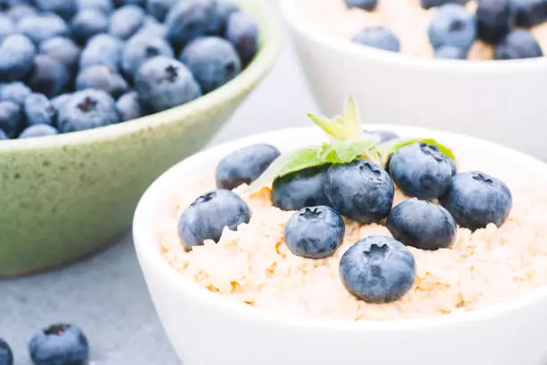 Photo of Closeup view of oatmeal porridge served with blueberry and mint leaves in white bowl on the table. Morning superfood porridge recipe. Healthy breakfast ideas