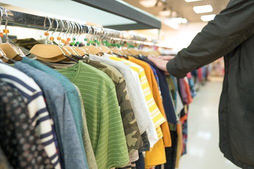 Man shopping at clothes marketshop. Mew fashion collection at fashionable clothes store. Clothing rental or thrift shopping concept. Secondhand store with clothes on hangers