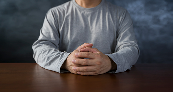 Interlocked fingers, white male hands interlocked on black rustic wood table close up. front view. a man is waiting for negotiations. Listening to a meeting panoramic image