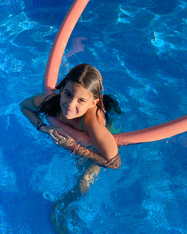 Smiling girl swimming in the pool with a floatation device flexible strong noodle swim support