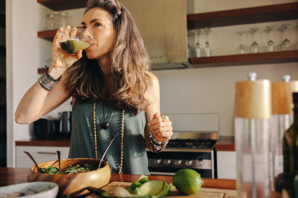 vegane frau trinkt grünen saft in ihrer küche - fruit salad fruit healthy eating making stock-fotos und bilder
