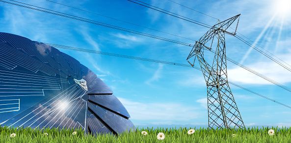 Solar panel and a high voltage tower on a green meadow (green grass and daisy flowers) against a blue sky with clouds and sunbeams.