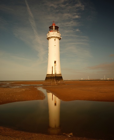 The New Brighton Lighthouse reflecting on the water surrounded by sand under a blue sky