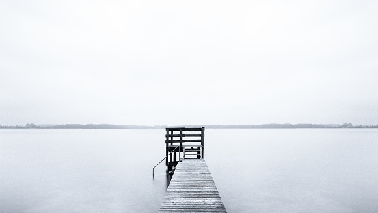 A foggy scenery of a pier leading to the ocean on a cold morning