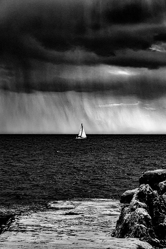 A greyscale of a sailing ship on the sea under a dark cloudy sky during daytime