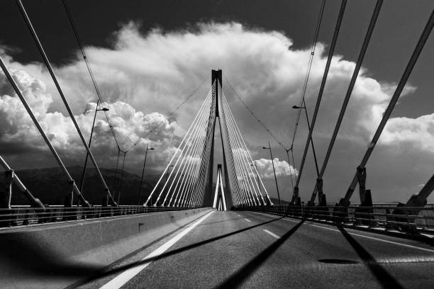 istock Greyscale of a Cable-stayed bridge with mountains on the background under a cloudy sky 1438904265