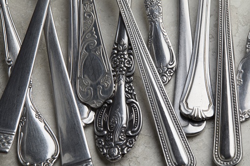 A lot of silver forks and spoons with antique patterns on a white surface