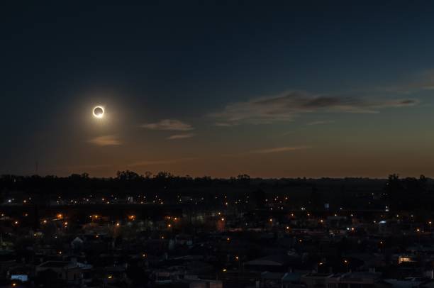 totale sonnenfinsternis am abend über einer von bäumen und gebäuden umgebenen stadt - eklipse stock-fotos und bilder