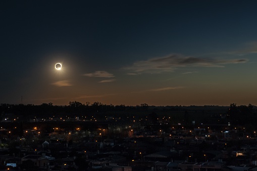 A total solar eclipse during the evening above a town surrounded by trees and buildings