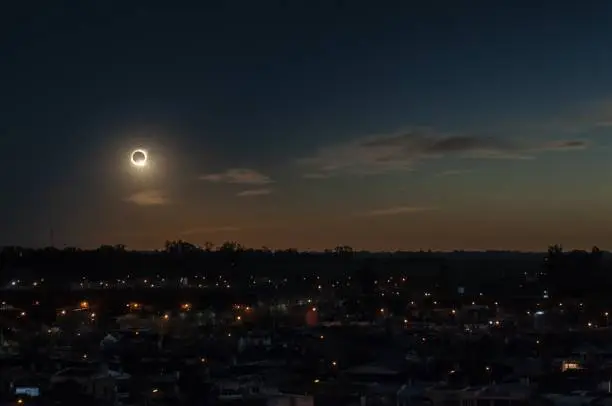 Photo of Total solar eclipse during the evening above a town surrounded by trees and buildings